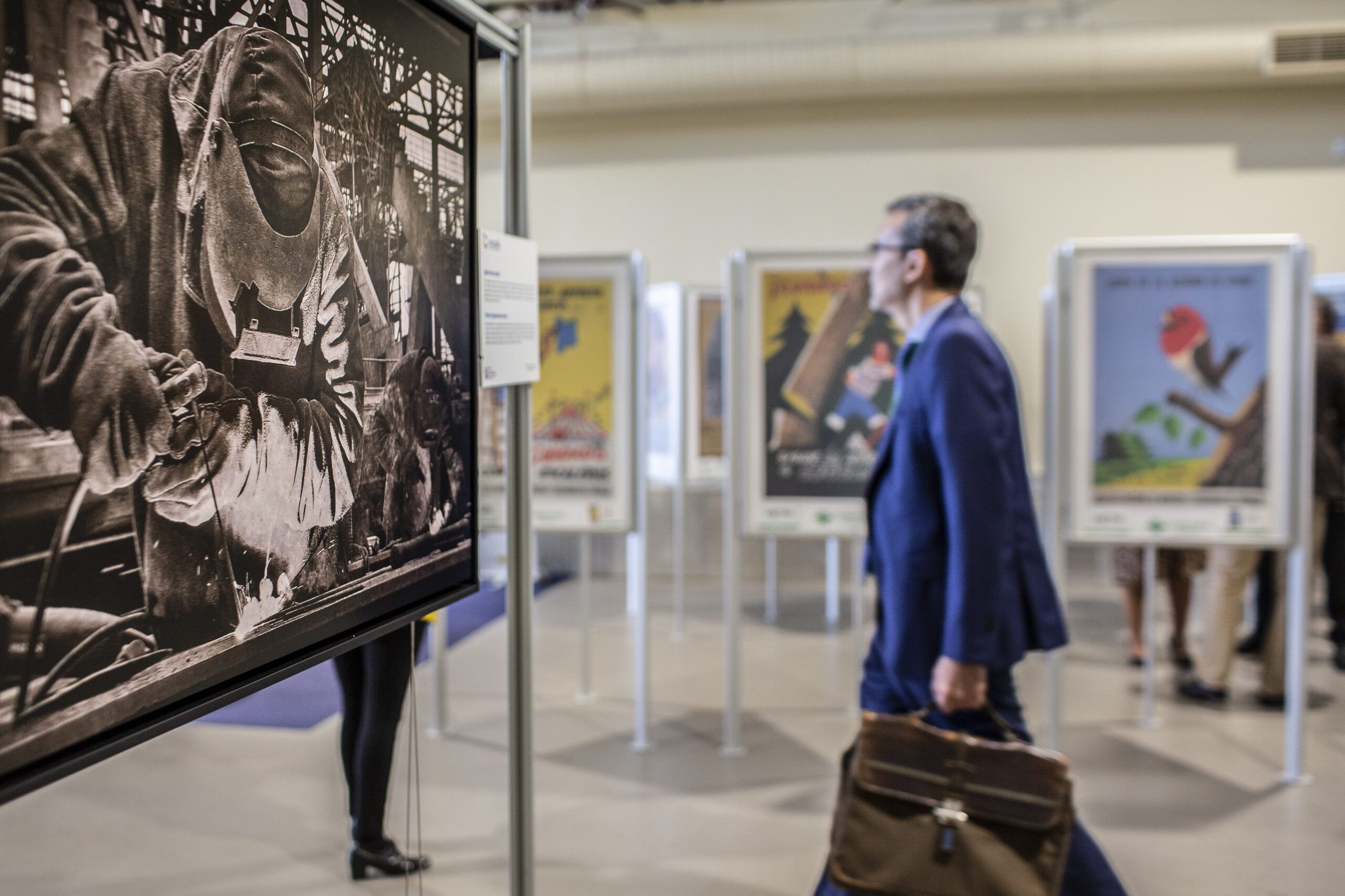 Hombre observa una exposición de carteles históricos sobre prevención laboral
